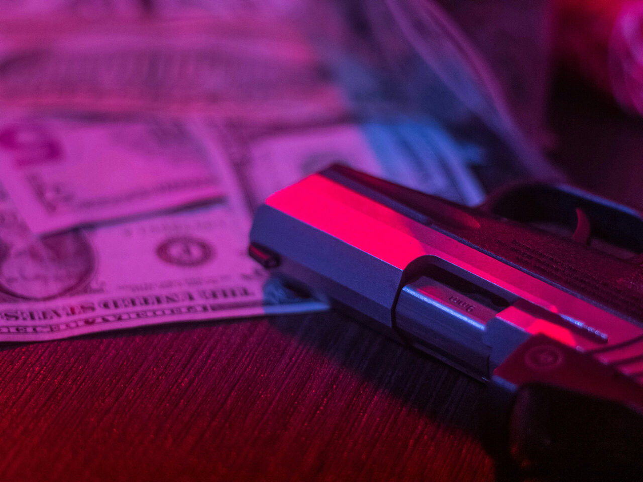 Handgun with cash on surface in purple and red lighting