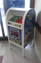 Project Medicine Drop prescription drug collection box mounted in police department lobby showing secure metal mailbox with program logos