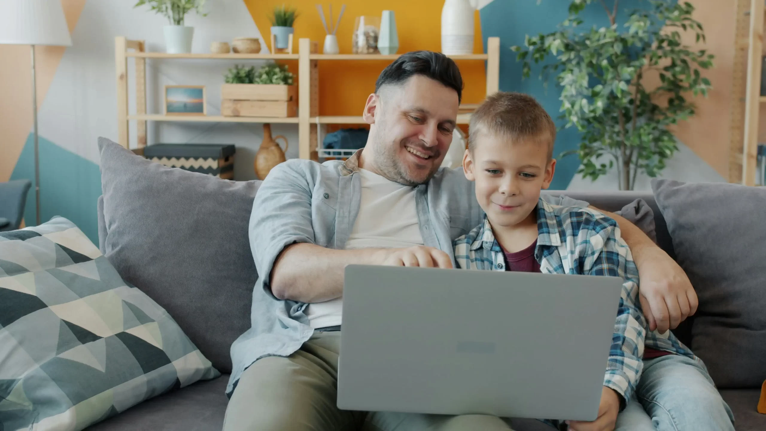 Father and son using laptop together on couch
